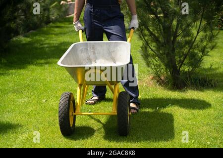 Ein junger Mann mit Händen in Handschuhen trägt einen metallenen Gartenwagen Stockfoto