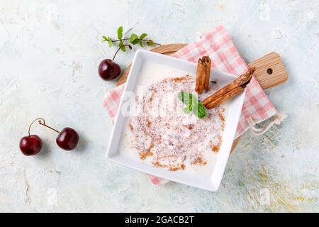 Hausgemachter Reispudding mit Zimt und Kirschen in einer weißen Schüssel auf Holz Stockfoto