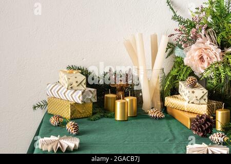 Festlich geschmückte Weihnachts- und Neujahrstisch, Tannenzweige und dekorative Blumen, Kerzen und goldene Geschenkschachteln, Baumdekorationen Tannenzapfen Stockfoto