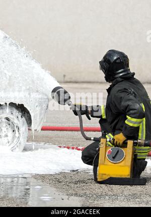 Tapferer Feuerwehrmann, der ein Autofeuer mit einem speziellen weißen, schwer entflammbaren Schaum löscht Stockfoto