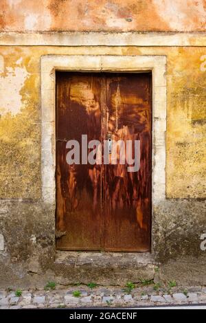 Eine alte rostige Tür in der bemalten Wand eines Dorfhauses in der kleinen Stadt Vila Facaia in Zentralportugal Stockfoto