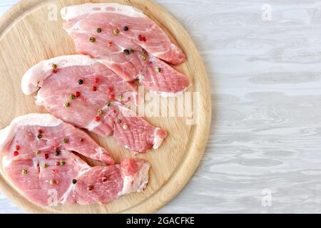 Rohe Schweinekoteletts, gewürzt mit verschiedenen Paprika auf einem Holzschneidebrett Stockfoto