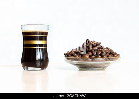 Schwarzer Kaffee im Glas und geröstete Kaffeebohnen auf Holztisch auf weißem Hintergrund Stockfoto