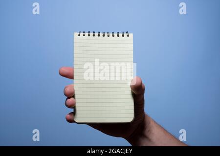 Ein Notizblock in der Hand eines Mannes mit blauem Hintergrund Stockfoto