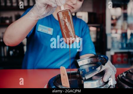 Ein Eisverkäufer taucht einen Popsicle in flüssige Schokolade. Stockfoto