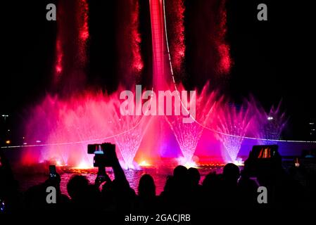 Die Menschenmenge fasziniert mit der Show des musikalischen Brunnens Silhouetten von Menschen von hinten werden am Telefon gefilmt Stockfoto