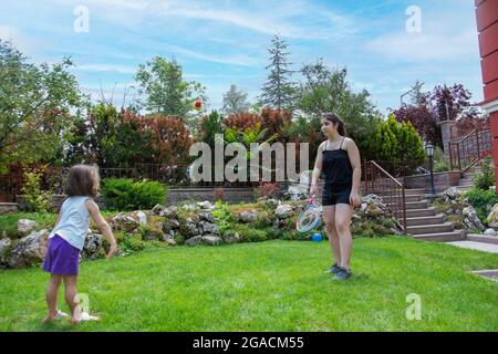 Das Teenager-Mädchen und ihre kleine Schwester spielen mit Tennisschläger und Ball im Garten Stockfoto
