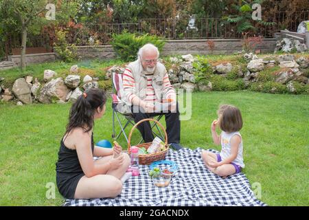 Die Mädchen picknicken mit ihren Großeltern. Der alte Mann sitzt auf dem Stuhl. Stockfoto