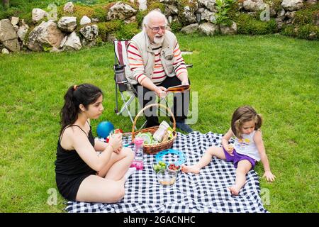 Die Mädchen picknicken mit ihren Großeltern. Der alte Mann sitzt auf dem Stuhl. Stockfoto
