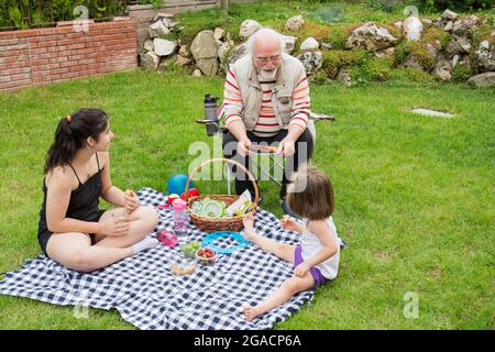 Die Mädchen picknicken mit ihren Großeltern. Der alte Mann sitzt auf dem Stuhl. Stockfoto