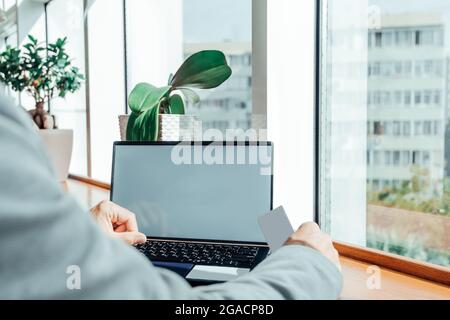 Nahaufnahme Foto Mann zeigt Blank White Visitenkarte und mit modernen Laptop auf Holz Tisch verschwommen Hintergrund. Mockup bereit für private Informationen. Stockfoto