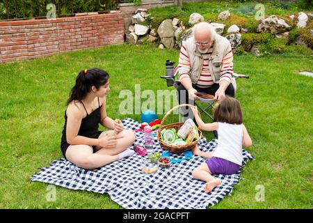 Die Mädchen picknicken mit ihren Großeltern. Der alte Mann sitzt auf dem Stuhl. Stockfoto