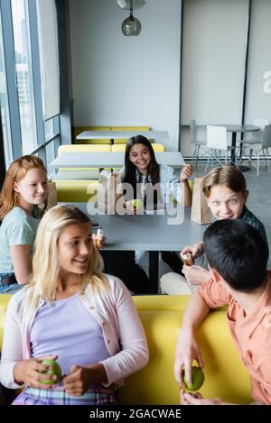 Fröhliche Teenager unterhalten sich während der Mittagspause im Schullokal Stockfoto