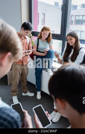 Teenager, die Geräte im Schulkorridor auf verschwommenem Vordergrund benutzen Stockfoto