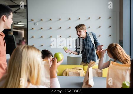 Fröhlicher Junge gestikuliert, während er mit Klassenkameraden im Schulrestaurant sprach Stockfoto