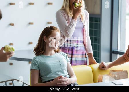 Rotschopf Schulmädchen lächelnd in der Nähe von Freunden essen Äpfel in der Schule Restaurant Stockfoto