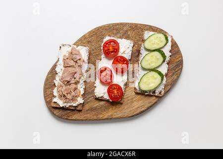 Köstlicher Toast mit knusprigem Brot mit verschiedenen Füllungen auf dem Tisch. Gurken, Tomaten, Frischkäse und Thunfisch sind Zutaten für Sandwiches. Stockfoto