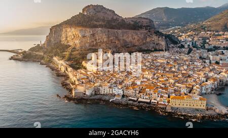 Sonnenaufgang über dem Hafen in Cefalu, Sizilien, Italien, Panorama-Luftaufnahme der Altstadt mit bunten Häusern am Wasser, Meer und La Rocca Klippe.attraktiv Stockfoto