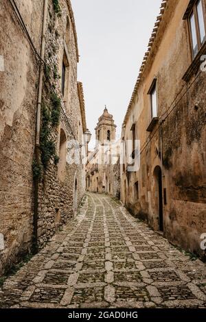 Schmale Straße in Erice mit San Martino Kirchturm, Sizilien, Italien. Historisches Zentrum des italienischen Dorfes. Erstaunliche mittelalterliche mediterrane Steingebäude Stockfoto