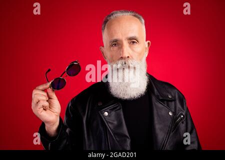 Portrait von attraktiven ernst grauhaarigen Mann hält in der Hand specs schönen Blick isoliert über hellen roten Hintergrund Stockfoto