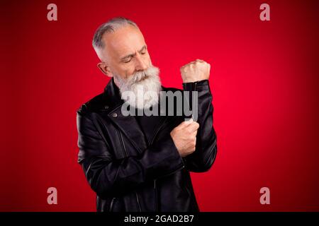 Portrait von attraktiven ernst grauhaarigen Mann Zipping Ärmel Jacke Dressing isoliert über hellen roten Hintergrund Stockfoto