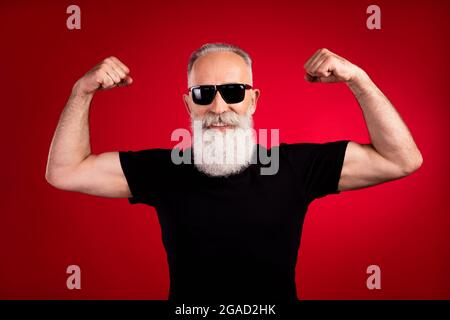 Porträt eines attraktiven älteren Rentners mit starkem, fröhlichen grauhaarigen Mann, der Muskeln zeigt, die auf einem hellroten Hintergrund isoliert sind Stockfoto