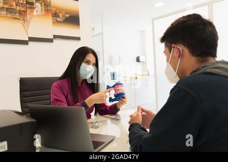 Junger Mann in einer Zahnarztpraxis mit allen Biosicherheitsmaßnahmen, Beratung durch einen Zahnarzt. Stockfoto