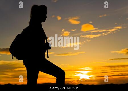 Frau, die in der Dämmerung auf dem Gipfel des Berges mit Sonnenstrahl unter ihren Füßen geht Stockfoto