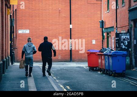 MANCHESTER, VEREINIGTES KÖNIGREICH - 18. Jul 2021: Eine Rückansicht von zwei Männern, die in einer Manchester Gasse in Großbritannien spazieren Stockfoto