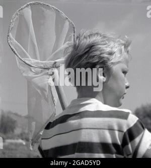 1960er, historisch. Sommerzeit und draußen auf dem Land, ein Junge mit seinem Schmetterlingsnetz. Stockfoto