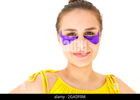 Junge, schön lächelnde Brünette Frau, die violette Kollagen-Flecken in Form von Sternschnuppen unter den Augen anwendet und Falten und dunkle Kreise entfernt. Femal Stockfoto