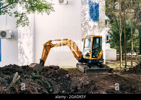 Der gelbe Bagger gräbt den Boden, um Rohre vor dem Haus zu verlegen Stockfoto