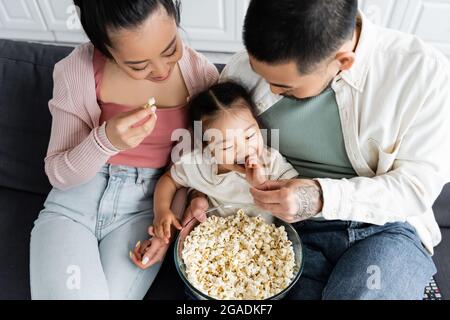 Blick von oben auf die glückliche asiatische Familie, die Popcorn im Wohnzimmer isst Stockfoto