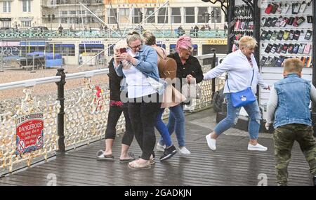 Brighton UK 30. Juli 2021 - Diese Besucher brüllen, als sie vom Spray aus dem Meer am Brighton Palace Pier gefangen werden, während Sturm Evert durch das Land fegt, mit Windgeschwindigkeiten, die in einigen Gegenden bis zu 60 km/h erreichen werden : Credit Simon Dack / Alamy Live News Stockfoto