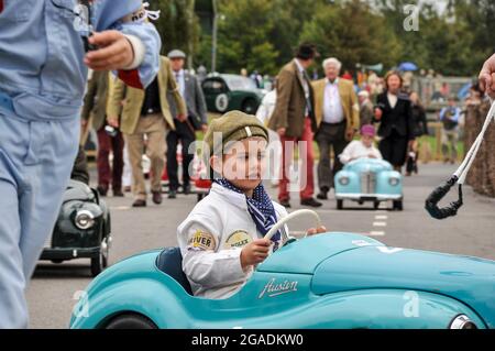 Settrington Cup Kinderrennfahrer in Austin J40 Pedalwagen beim Goodwood Revival, der den Montagebereich verlässt, um zu Rennen. Fahrer und Eltern Stockfoto