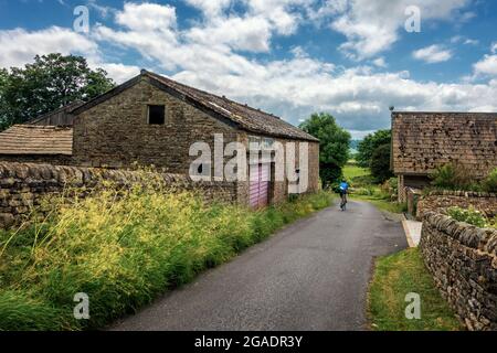 Radfahrer radeln auf einer Landstraße zwischen alten Steinbauernhäusern, Stainburn, North Yorkshire, Großbritannien Stockfoto