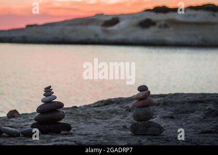 Pyramidensteine balancieren auf dem Sand des Strandes. Das Objekt befindet sich im Fokus, in der Sonnenuntergangsansicht. Stockfoto