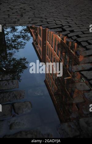 Dunkle, verlassene Kopfsteinpflasterstraße mit einer Pfütze, die Mietshäuser in der Crosby Street, SOHO, in New York City widerspiegelt. Pfützen Geschichten Serie. Stockfoto