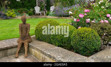 Willow Skulptur Kunst (ornamental Feature) in schönen bunten Landschaftsgarten (blühende Pflanzen, Box Kugeln, Rasen, Stühle) - Yorkshire England UK. Stockfoto