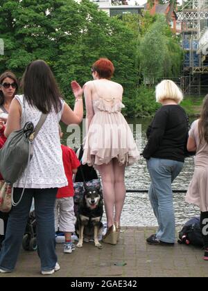 Eine große junge rotköpfige Frau am Flussufer in Chester, Cheshire, England. Sie trägt ein stilvolles kurzes Kleid und High Heels. Sie hat einen Hund an der Leine Stockfoto