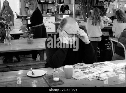 Ein älterer Mann sitzt in einem Café in Shrewsbury mit einer Tasse Kaffee. Er liest eine Zeitung. Monochrome Fotografie Stockfoto