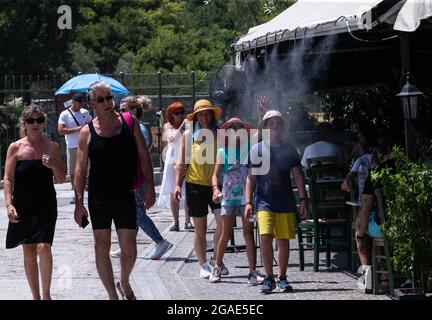 Athen, Griechenland. Juli 2021. Am 30. Juli 2021 werden Menschen unter einem Wassersprühsystem vor einer Cafeteria in Athen, Griechenland, abgekühlt. Griechische Meteorologen warnten am Donnerstag, dass das Land in den nächsten zehn Tagen eine intensive und anhaltende Hitzewelle erleben wird. Nach Angaben des Hellenischen Nationalen Meteorologischen Dienstes (EMY) könnten die Temperaturen auf dem griechischen Festland 44 Grad Celsius erreichen. UM MIT einer „intensiven Hitzewelle zu gehen, die Griechenland in den kommenden Tagen versengen soll, warnen Meteorologen“ Kredit: Marios Lolos/Xinhua/Alamy Live News Stockfoto