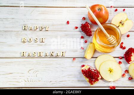 Happy Rosh Hashanah. Inschrift auf einem hölzernen Hintergrund. Traditionelle Symbole der Feier. Äpfel, Granatäpfel und Honig. Stockfoto