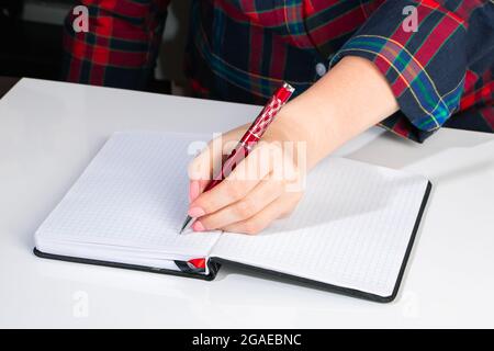 Die junge Frau hält einen Stift in der linken Hand und schreibt eine Notiz in ein leeres Notizbuch. Internationaler Tag Der Linken Stockfoto