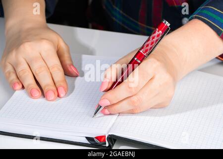 Frau schreibt in ein Notizbuch und hält mit der linken Hand einen Stift. Das Mädchen arbeitet im Büro. Tag der Linken am 13. August. Stockfoto