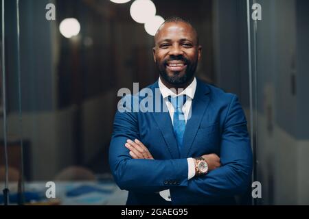Portrait lächelnder afroamerikanischer Geschäftsmann in blauem Anzug im Büro. Stockfoto
