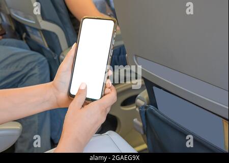 Frau, die im Flugzeug sitzt und ein Handy mit Mockup verwendet. Frau mit Smartphone im Flugzeug während des Fluges. Mockup Bild von Frauen Hände halten ein b Stockfoto