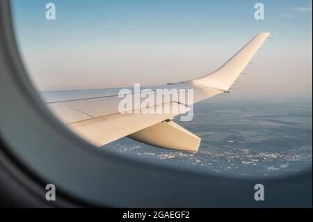 Blick durch das Fenster aus der Flugzeugkabine. Blick auf den Himmel von der Kabinenbesatzung aus durchsichtigen Glasfenstern bis zum Flugzeugflügel des Flugzeugs. Internationale Fracht Stockfoto