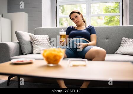 Übermäßiges Essen mit Junk Food, Bier trinken und Fernsehen Stockfoto