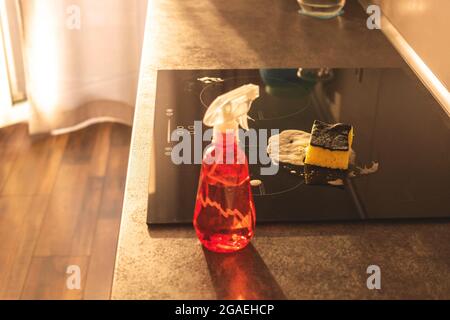 Bereit für die Reinigung der Wohnküche, Spray Waschmittelflasche und gelben Schwamm auf der Tischplatte und Elektroherd, moderne Küche Interieur Stockfoto